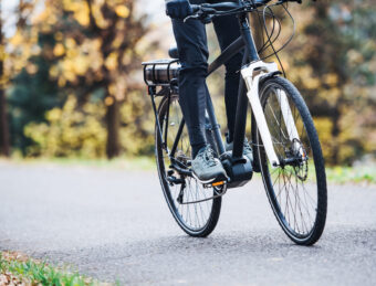 An unrecognizable man on electrobike cycling outdoors on a road in park.
